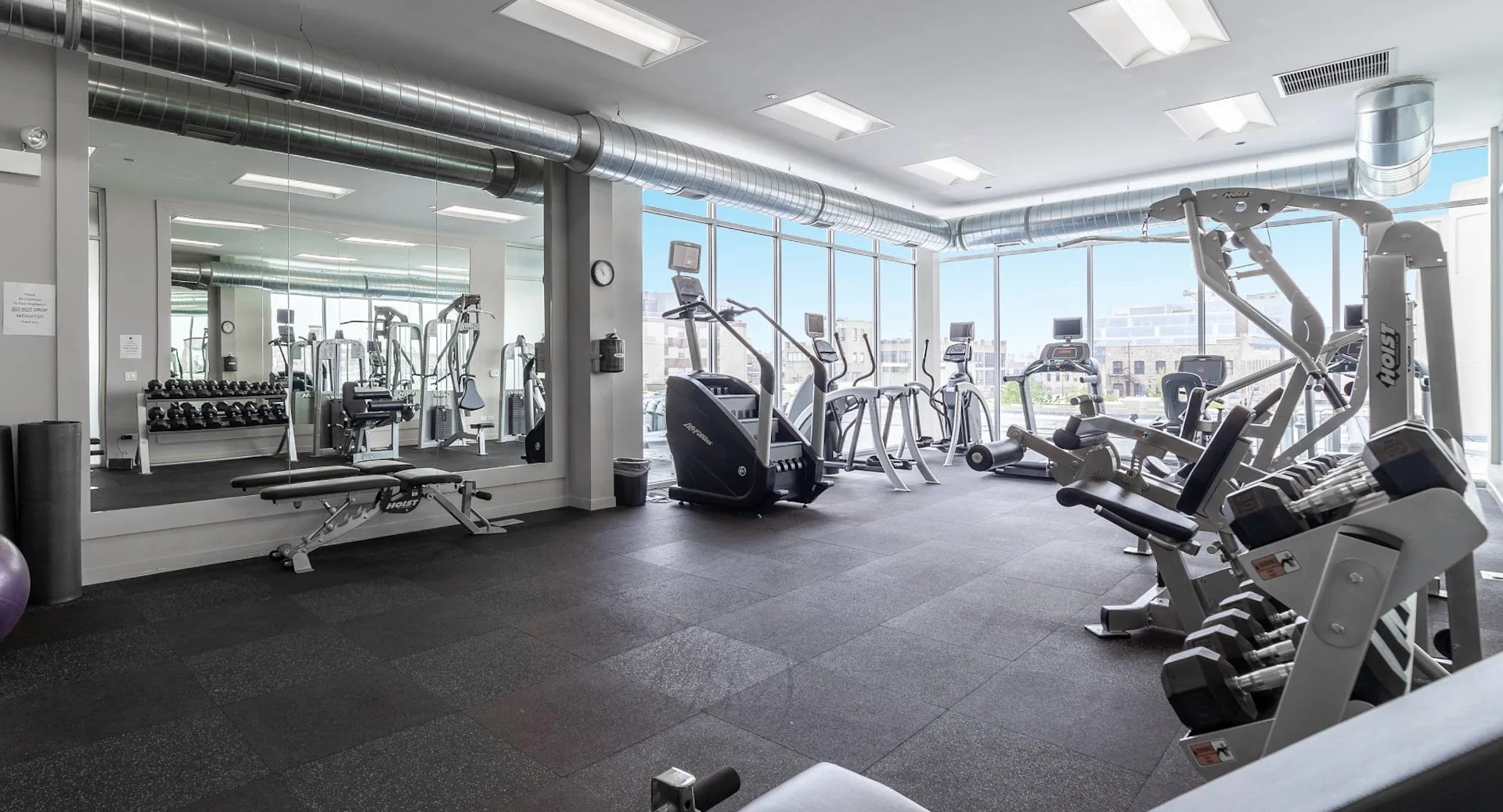 Bright fitness center at 13thirteen Randolph Street Lofts featuring treadmills, ellipticals, free weights, and mirrors with skyline views for Chicago renters
