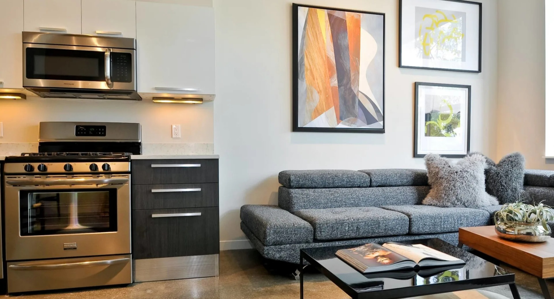 Open-concept living room and kitchen at 13thirteen Randolph Street Lofts featuring stainless appliances, gray sectional, and modern art in Chicago