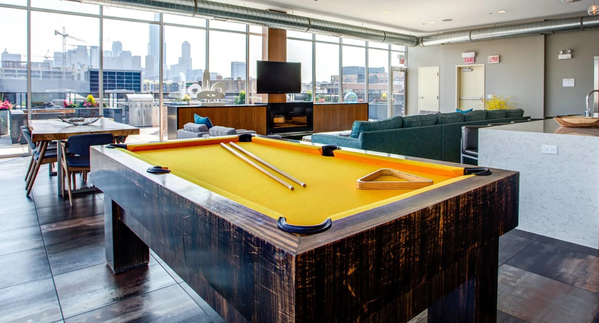 Spacious resident clubroom at 13thirteen Randolph Street Lofts featuring a pool table, TV lounge, chef’s island kitchen, and floor-to-ceiling windows