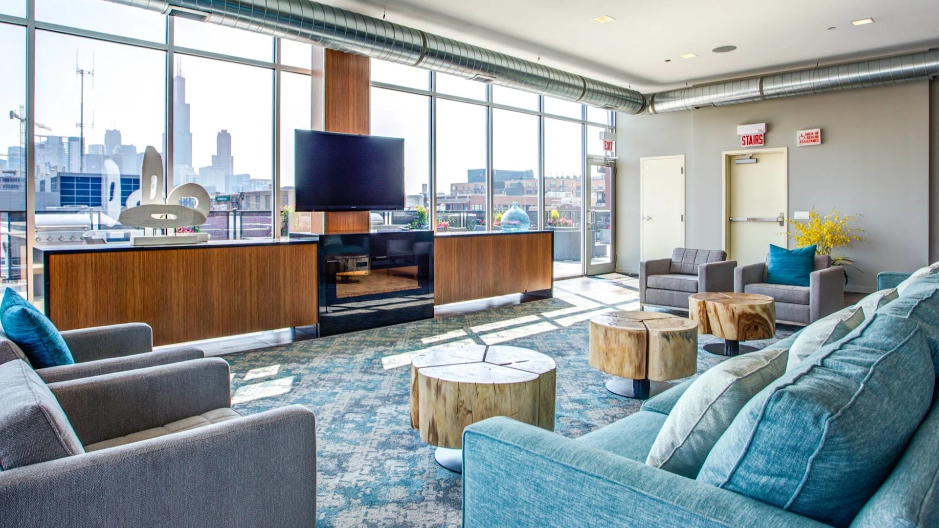 Modern resident lounge at 13thirteen Randolph Street Lofts with plush seating, TV, fireplace feature, and expansive windows overlooking downtown Chicago