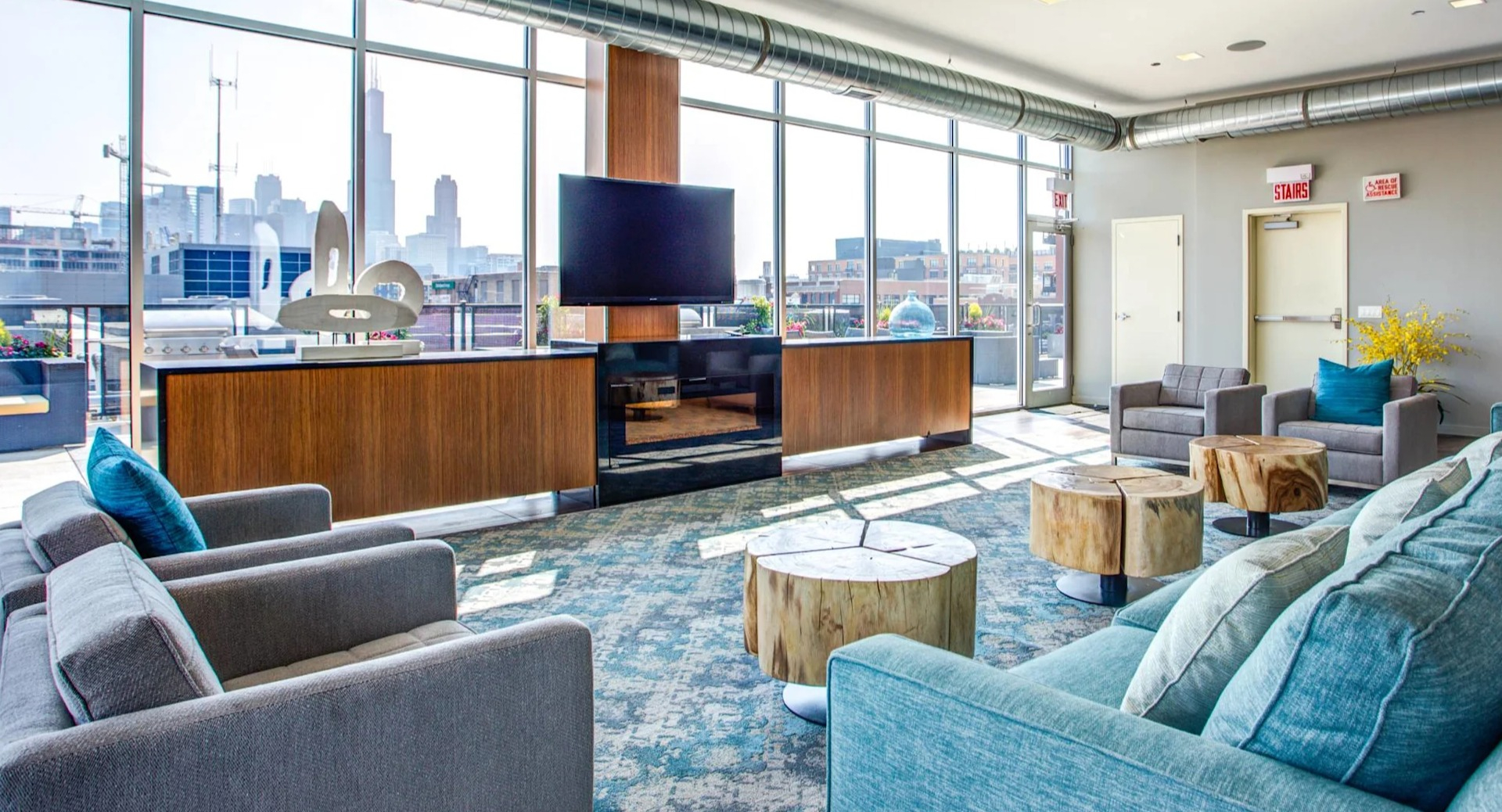 Modern resident lounge at 13thirteen Randolph Street Lofts with plush seating, TV, fireplace feature, and expansive windows overlooking downtown Chicago