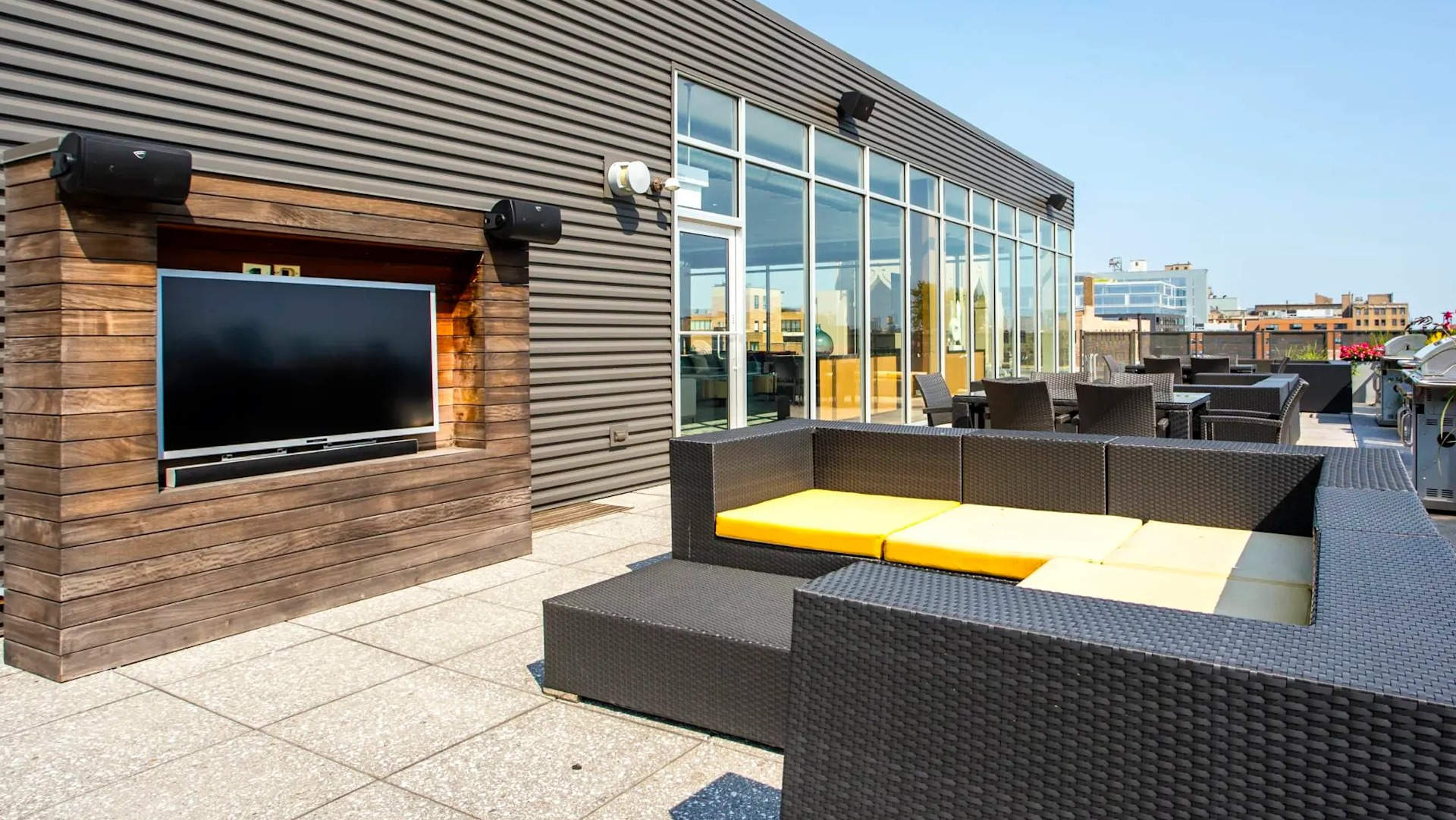 Rooftop lounge at 13thirteen Randolph Street Lofts with outdoor TV, wicker seating, grills, and city views—ideal for relaxing or game nights in Chicago
