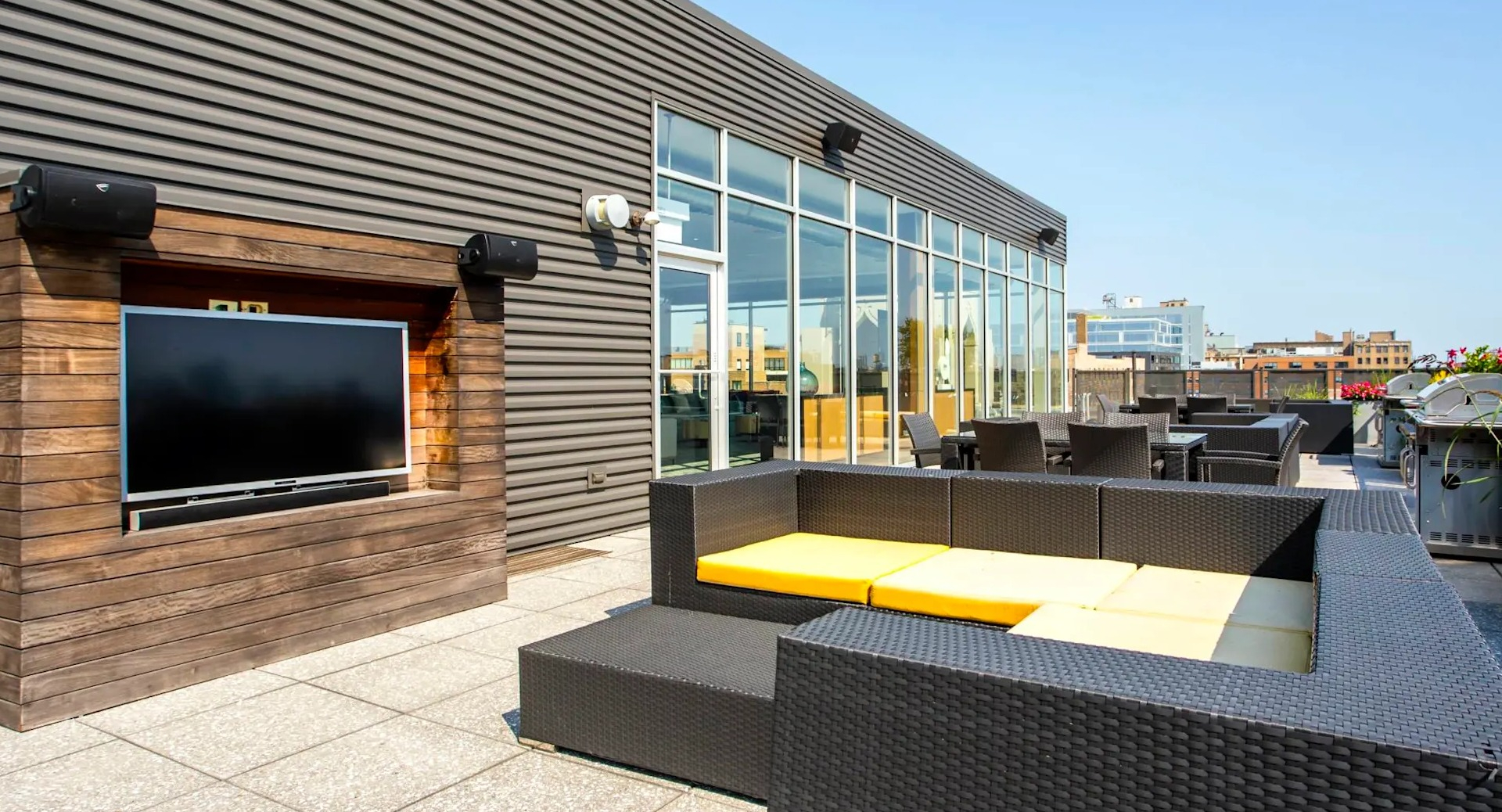 Rooftop lounge at 13thirteen Randolph Street Lofts with outdoor TV, wicker seating, grills, and city views—ideal for relaxing or game nights in Chicago