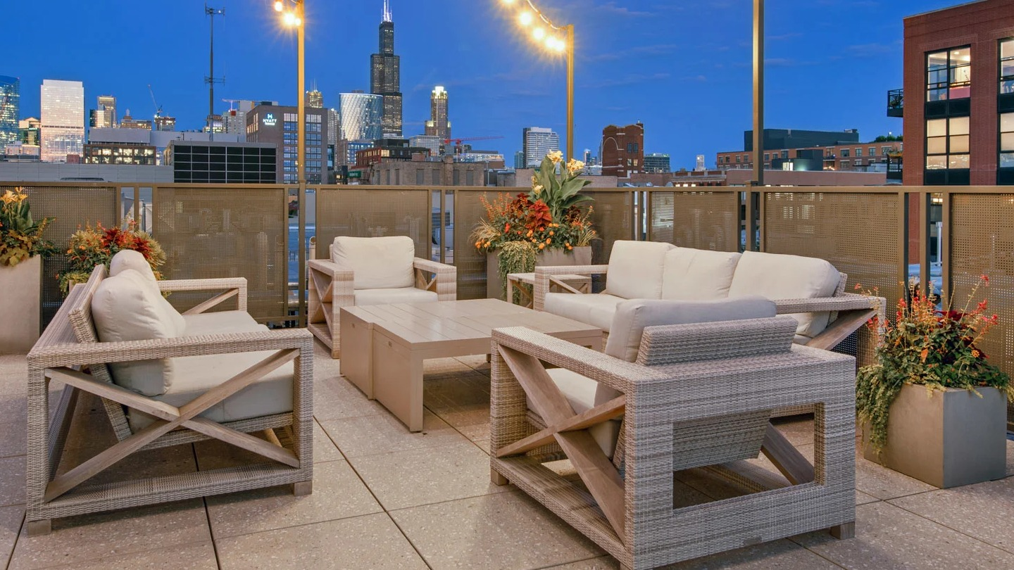 Cozy rooftop lounge at 13thirteen Randolph Street Lofts with cushioned seating, planters, and string lights framing stunning nighttime Chicago skyline views