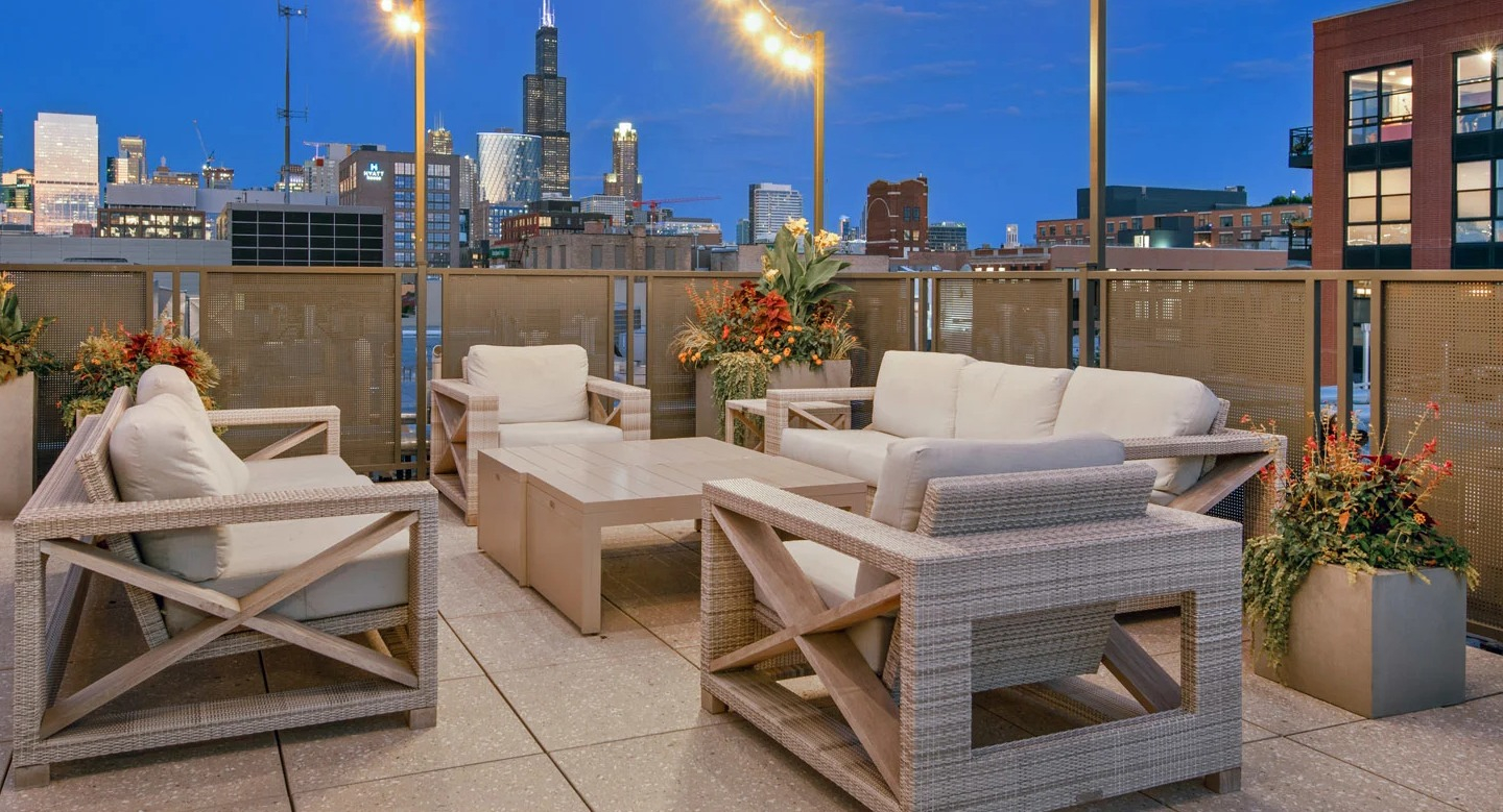 Cozy rooftop lounge at 13thirteen Randolph Street Lofts with cushioned seating, planters, and string lights framing stunning nighttime Chicago skyline views