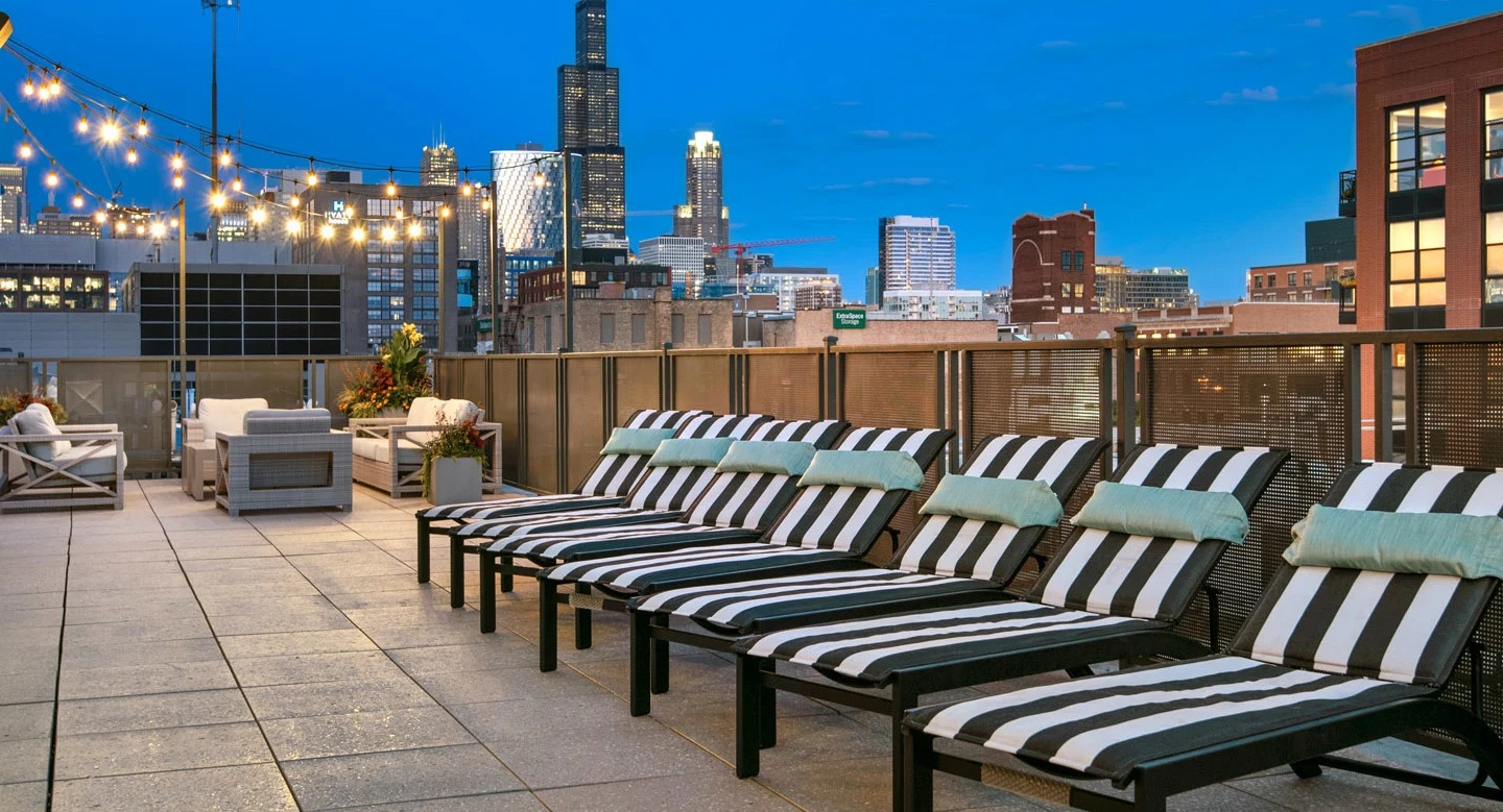 Evening sundeck at 13thirteen Randolph Street Lofts with striped loungers, string lights, and dramatic Chicago skyline views for relaxing after work