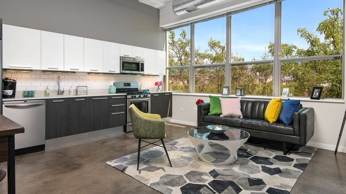 Spacious loft living room at 13thirteen Randolph Street Lofts with exposed ductwork, large windows, sleek kitchen, and modern furnishings in Chicago