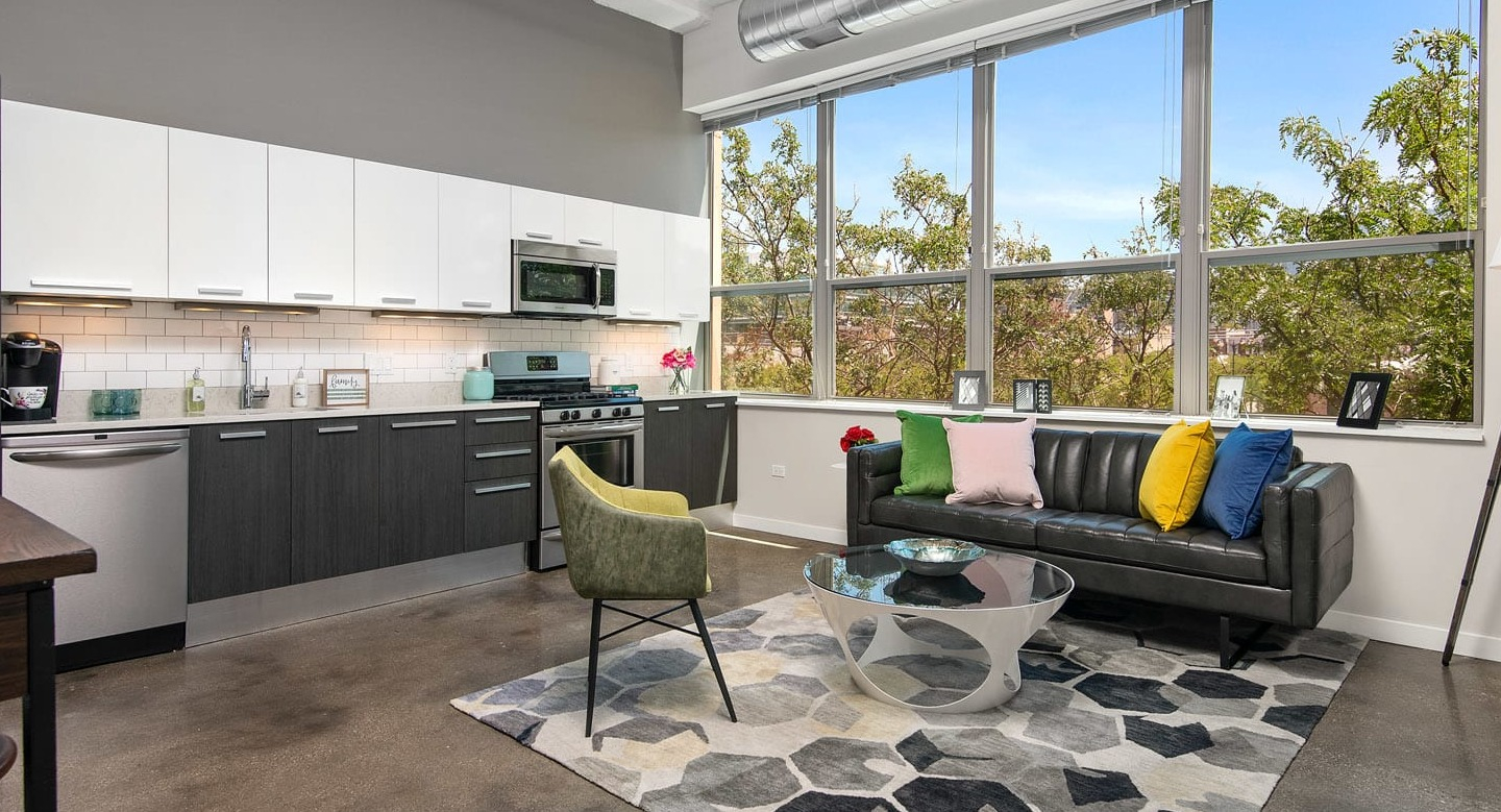 Spacious loft living room at 13thirteen Randolph Street Lofts with exposed ductwork, large windows, sleek kitchen, and modern furnishings in Chicago