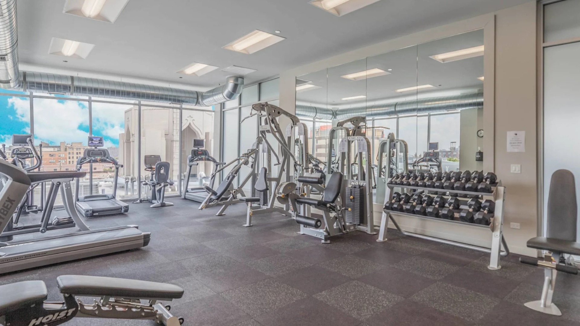 Strength training gym at 13thirteen Randolph Street Lofts with weight machines, dumbbells, and mirrored walls, offering residents an easy on-site workout