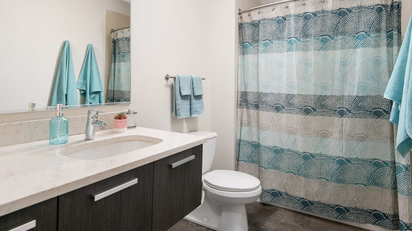 Updated bathroom at 13thirteen Randolph Street Lofts with long quartz vanity, large mirror, and shower-tub with patterned curtain for easy Chicago living