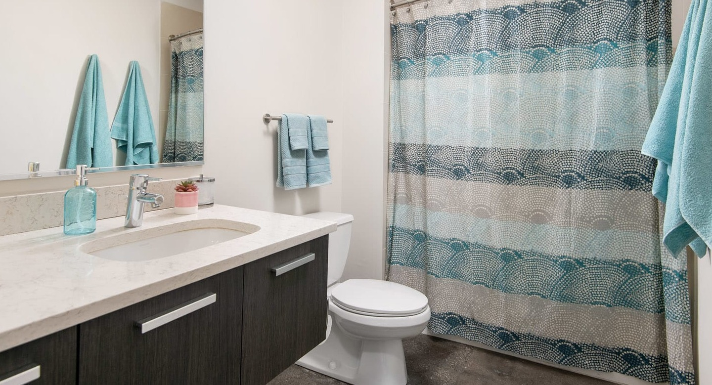Updated bathroom at 13thirteen Randolph Street Lofts with long quartz vanity, large mirror, and shower-tub with patterned curtain for easy Chicago living
