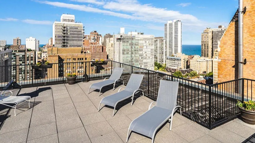 Expansive rooftop deck with lounge chairs and potted plants, showcasing a wide cityscape and blue skies at 14 West Elm Apartments in Chicago