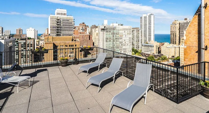 Expansive rooftop deck with lounge chairs and potted plants, showcasing a wide cityscape and blue skies at 14 West Elm Apartments in Chicago
