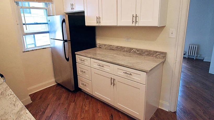 Recently renovated kitchen featuring white cabinets, granite countertops, and stainless steel refrigerator at 14 West Elm Apartments in Chicago