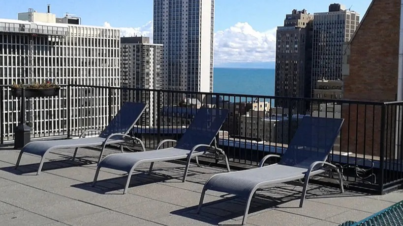 Rooftop lounge area with multiple chaise lounges, offering a stunning city skyline and lake view at 14 West Elm Apartments in Chicago