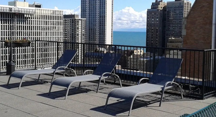 Rooftop lounge area with multiple chaise lounges, offering a stunning city skyline and lake view at 14 West Elm Apartments in Chicago