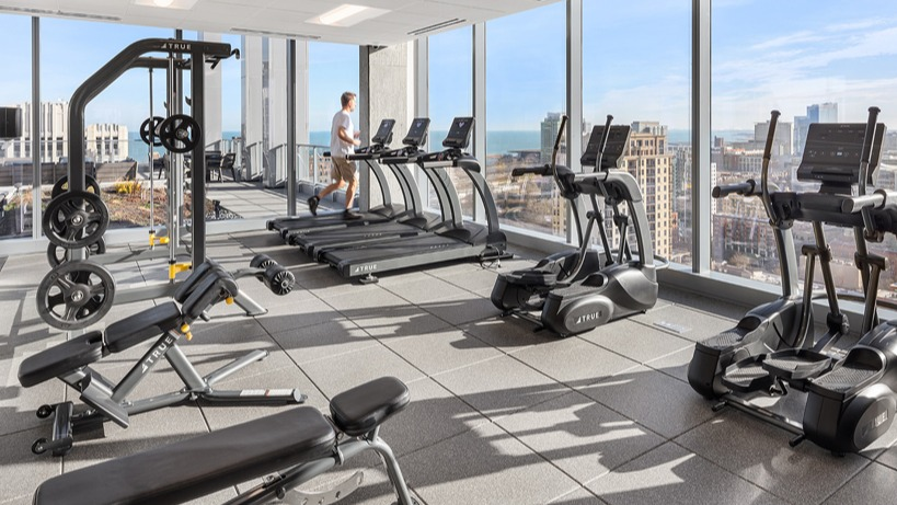 Fitness center with treadmills, strength machines, and expansive city and lake views through floor-to-ceiling windows at 1400 Wabash in Chicago