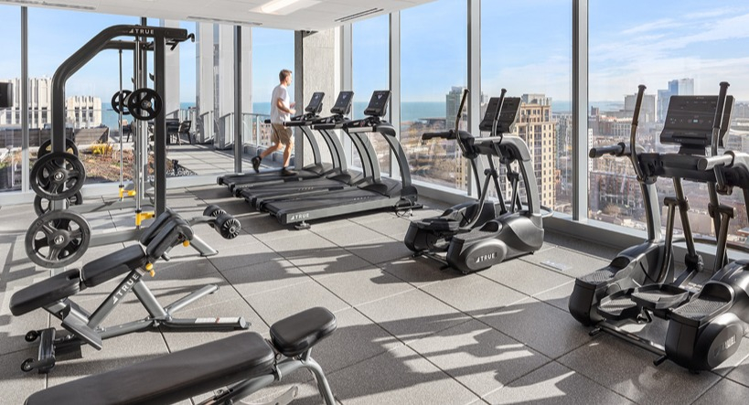 Fitness center with treadmills, strength machines, and expansive city and lake views through floor-to-ceiling windows at 1400 Wabash in Chicago
