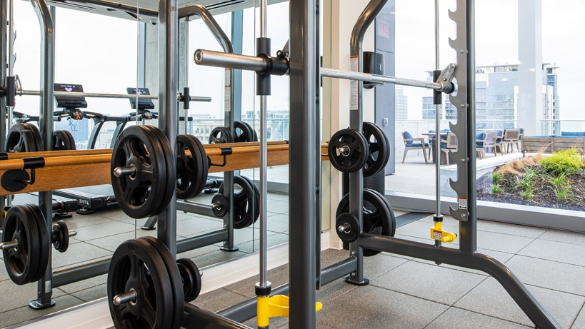 Fitness center weight room with Smith machine, mirrored wall, and cardio equipment beside floor-to-ceiling windows at 1400 Wabash apartments in Chicago