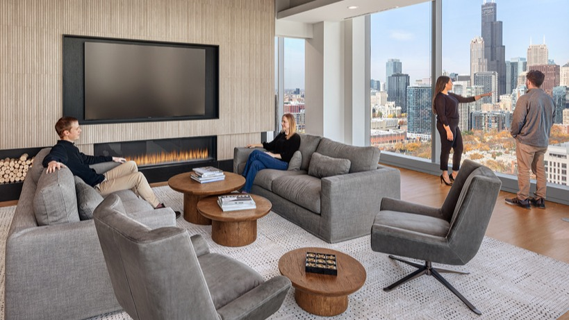 Sophisticated resident lounge with fireplace, plush seating, and panoramic skyline views through tall windows at 1400 Wabash apartments in Chicago