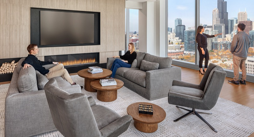 Sophisticated resident lounge with fireplace, plush seating, and panoramic skyline views through tall windows at 1400 Wabash apartments in Chicago