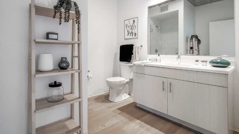 Bright bathroom with double vanity, quartz counters, open wood shelving, and a sleek glass shower at 1400 Wabash apartments in Chicago