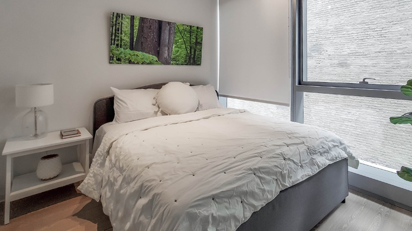Bright bedroom with queen bed, crisp white bedding, roller shades, and a large window bringing natural light at 1400 Wabash in Chicago