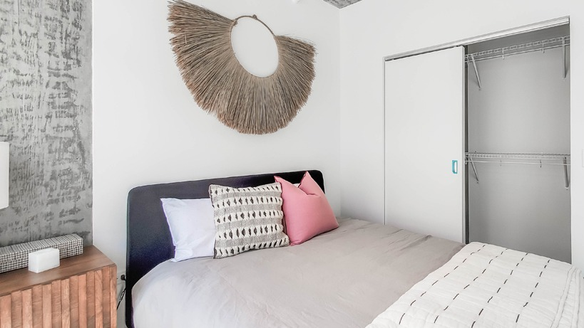 Cozy bedroom with textured concrete ceiling, layered bedding, wall art, and a sliding-door closet at 1400 Wabash apartments in Chicago