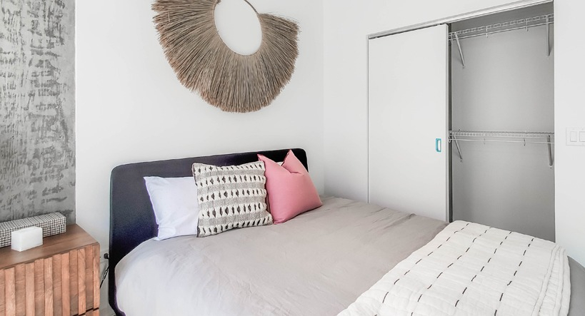 Cozy bedroom with textured concrete ceiling, layered bedding, wall art, and a sliding-door closet at 1400 Wabash apartments in Chicago