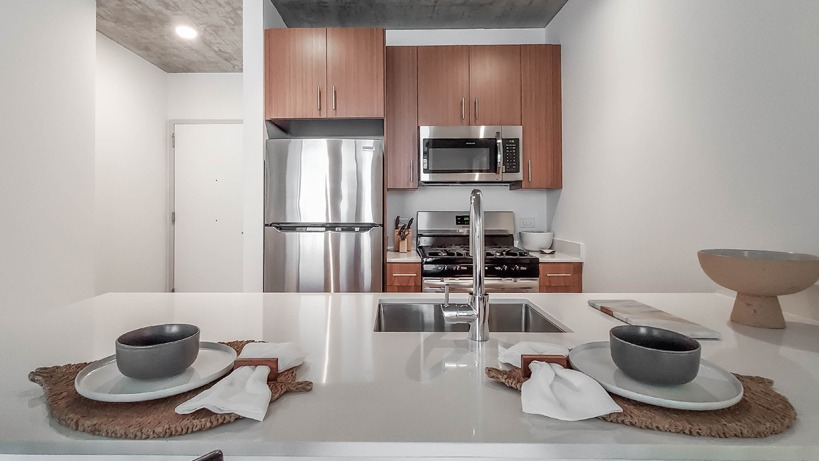 Contemporary kitchen with island seating, stainless steel appliances, and wood cabinets under an exposed concrete ceiling at 1400 Wabash in Chicago