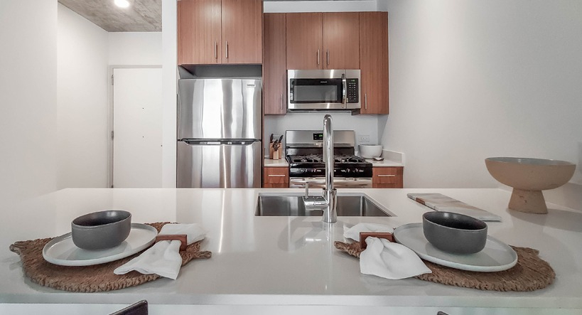 Contemporary kitchen with island seating, stainless steel appliances, and wood cabinets under an exposed concrete ceiling at 1400 Wabash in Chicago
