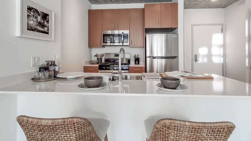 Modern kitchen with island seating, stainless steel appliances, and warm wood cabinets under an exposed concrete ceiling at 1400 Wabash in Chicago