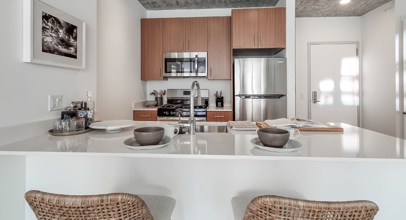 Modern kitchen with island seating, stainless steel appliances, and warm wood cabinets under an exposed concrete ceiling at 1400 Wabash in Chicago