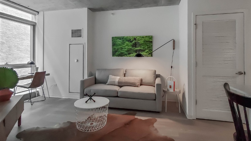 Cozy living room with gray sofa, wall-mounted lamp, cowhide rug, and a compact study nook at 1400 Wabash apartments in Chicago
