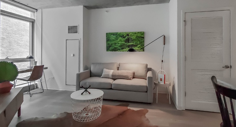 Cozy living room with gray sofa, wall-mounted lamp, cowhide rug, and a compact study nook at 1400 Wabash apartments in Chicago