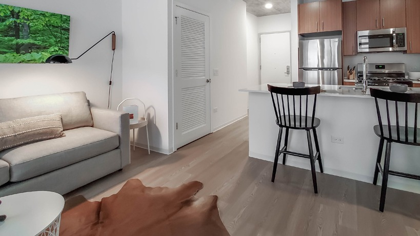 Open-concept living area connecting sofa seating and breakfast bar to the kitchen beneath an industrial concrete ceiling at 1400 Wabash in Chicago