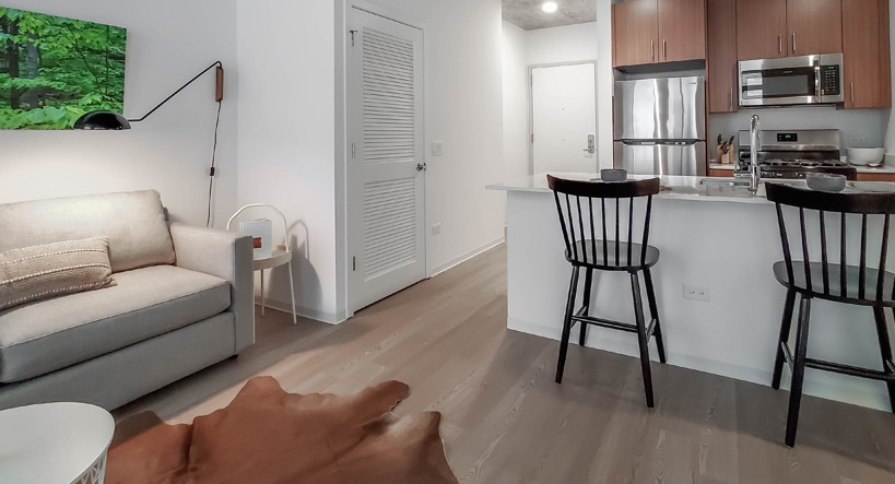 Open-concept living area connecting sofa seating and breakfast bar to the kitchen beneath an industrial concrete ceiling at 1400 Wabash in Chicago
