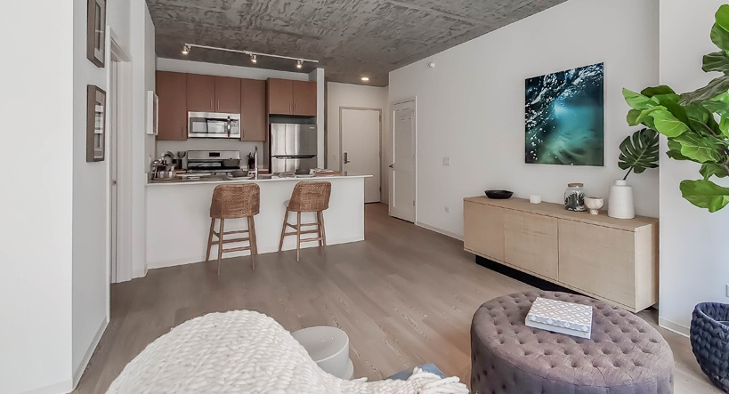 Spacious living room with large plant, media console, soft seating, and track lighting near the kitchen at 1400 Wabash apartments in Chicago