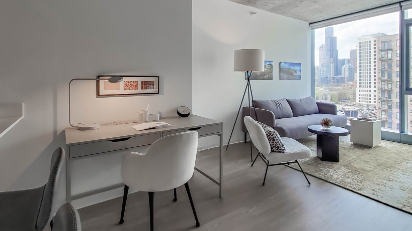 Open living and work area with desk, bar seating, and lounge space facing tall windows for natural light at 1400 Wabash apartments in Chicago