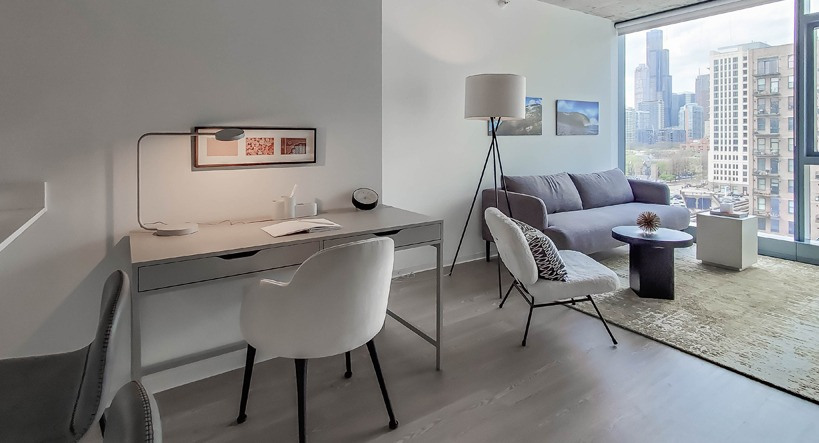 Open living and work area with desk, bar seating, and lounge space facing tall windows for natural light at 1400 Wabash apartments in Chicago