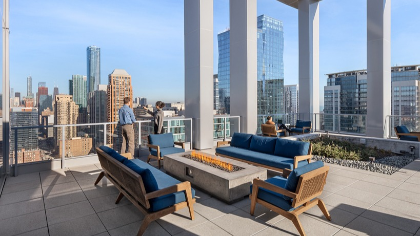 Rooftop deck lounge with blue cushioned sofas around a modern fire pit, tall frame columns, and sweeping skyline views at 1400 Wabash in Chicago