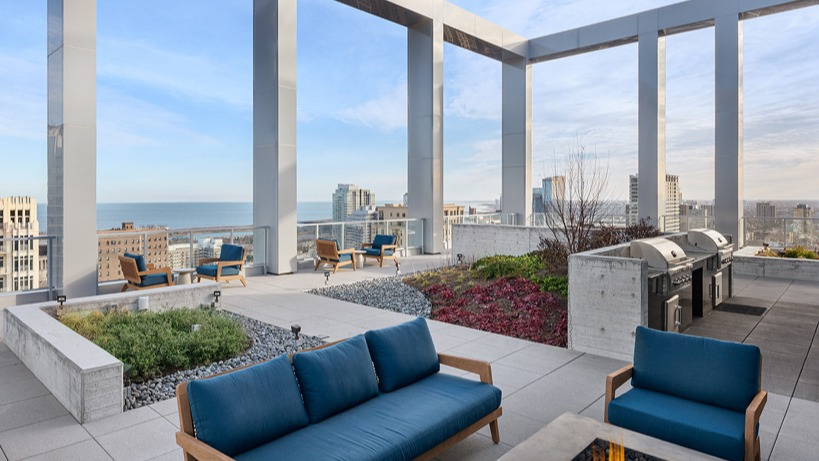 Rooftop seating clustered around a linear fire pit near outdoor grill stations, landscaped planters, and Lake Michigan views at 1400 Wabash in Chicago