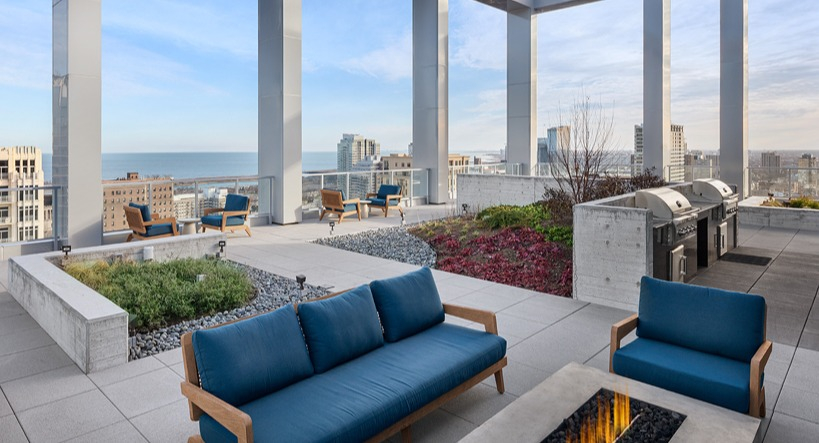 Rooftop seating clustered around a linear fire pit near outdoor grill stations, landscaped planters, and Lake Michigan views at 1400 Wabash in Chicago