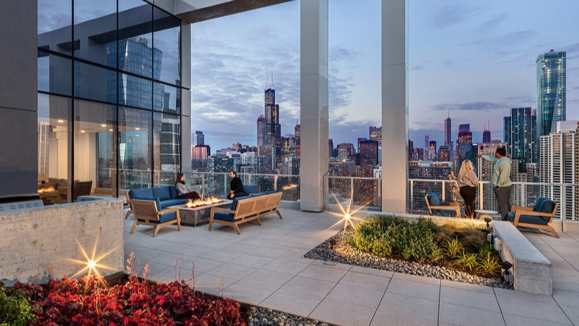 Rooftop terrace at dusk with glowing fire pits, landscaped planters, and dramatic views of the Chicago skyline at 1400 Wabash apartments