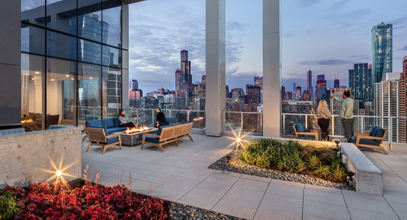 Rooftop terrace at dusk with glowing fire pits, landscaped planters, and dramatic views of the Chicago skyline at 1400 Wabash apartments