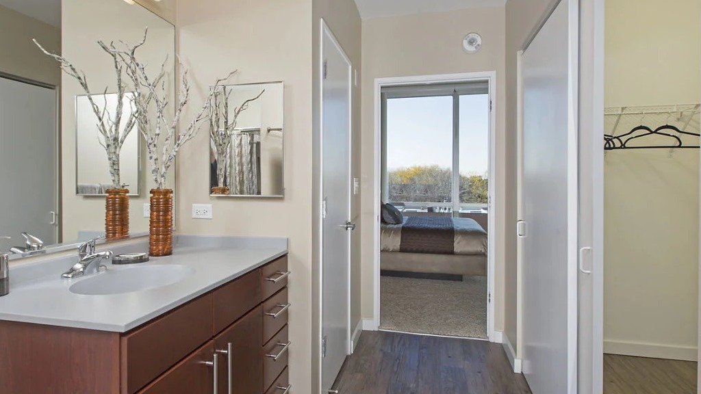 Modern bathroom at 1401 S. State Apartments in Chicago, featuring a sleek vanity, large mirror, and an adjacent walk-in closet