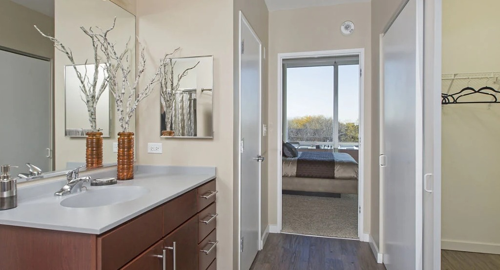 Modern bathroom at 1401 S. State Apartments in Chicago, featuring a sleek vanity, large mirror, and an adjacent walk-in closet