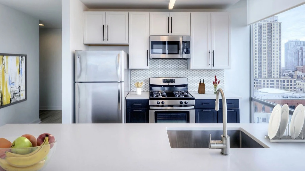 Modern apartment kitchen at 1401 S. State Apartments in Chicago, featuring white cabinetry, dark island, and stainless steel appliances