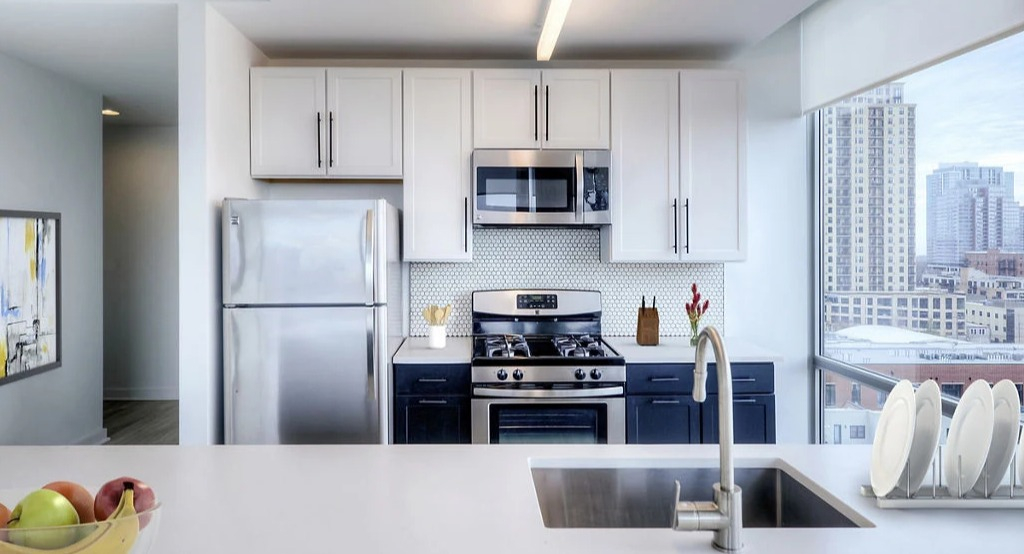 Modern apartment kitchen at 1401 S. State Apartments in Chicago, featuring white cabinetry, dark island, and stainless steel appliances