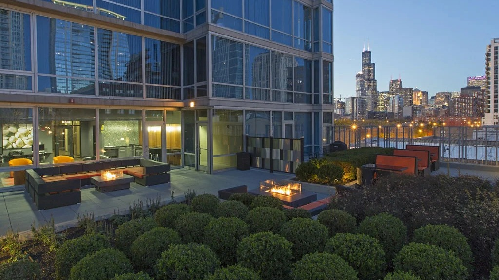 Luxurious rooftop terrace at 1401 S. State Apartments in Chicago, featuring fire pits, lounge seating, and a stunning city skyline at dusk